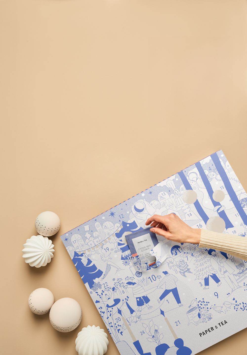 Blauer und weißer Adventskalender, Hand öffnet Tür Nummer 5, dekorative Kugeln daneben.