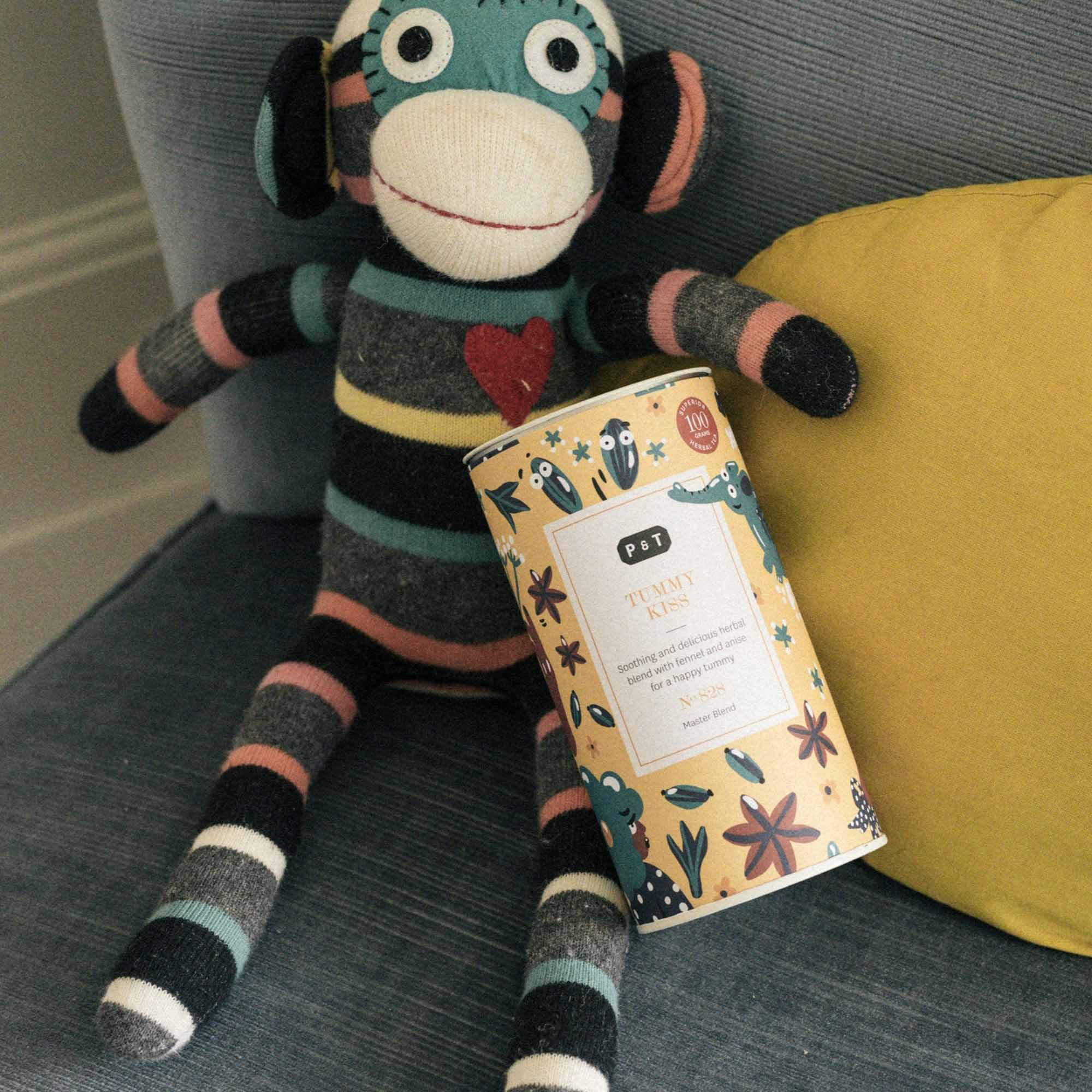 Gestricktes Sockenaffen-Spielzeug auf grauem Sofa hält P & T TUMMY KISS Dose mit Fenchel-Anis Kräutertee