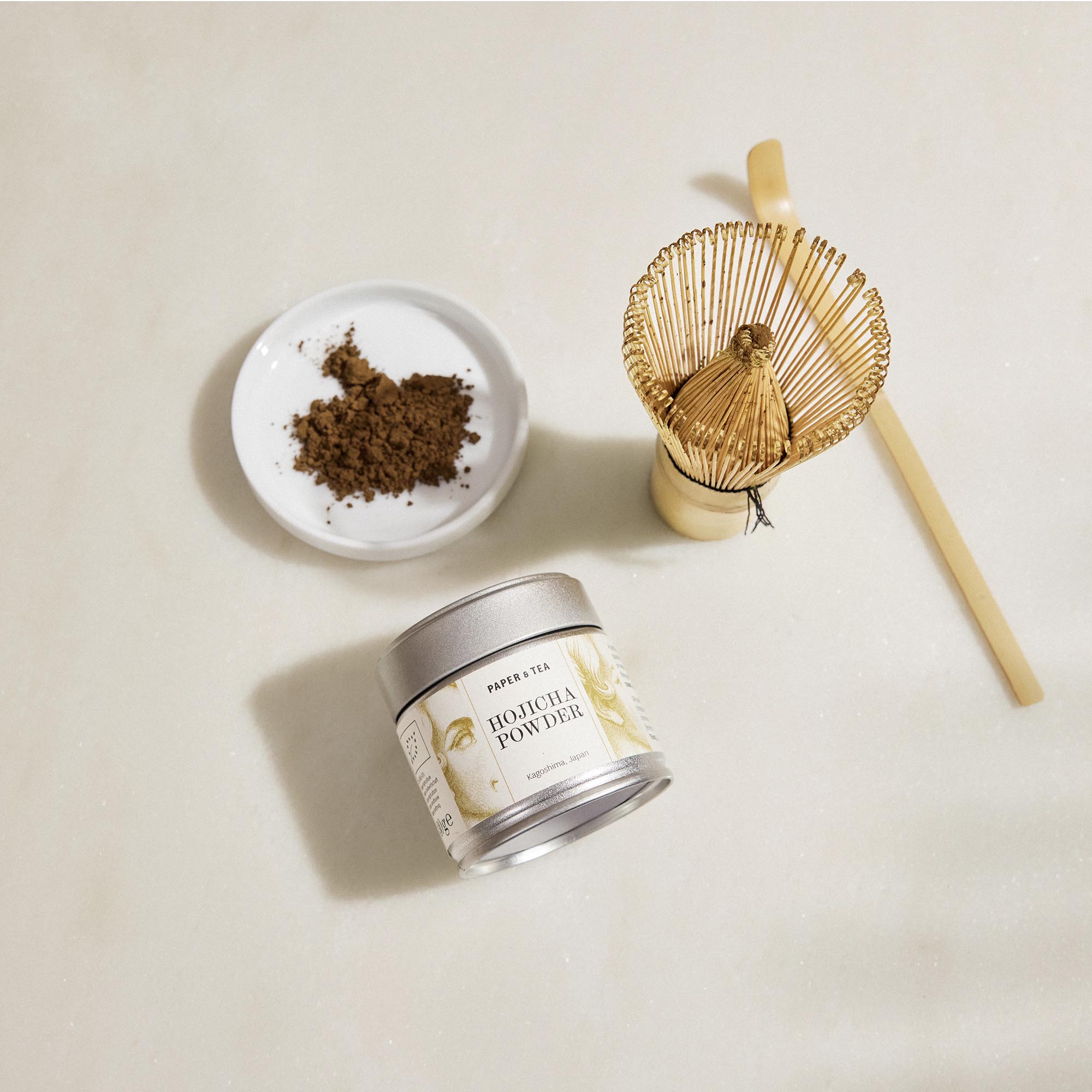 Kleiner Metallbehälter mit Paper & Tea Hojicha Pulver aus Kagoshima, braunes Pulver in Keramikschale, Bambusbesen, Teelöffel