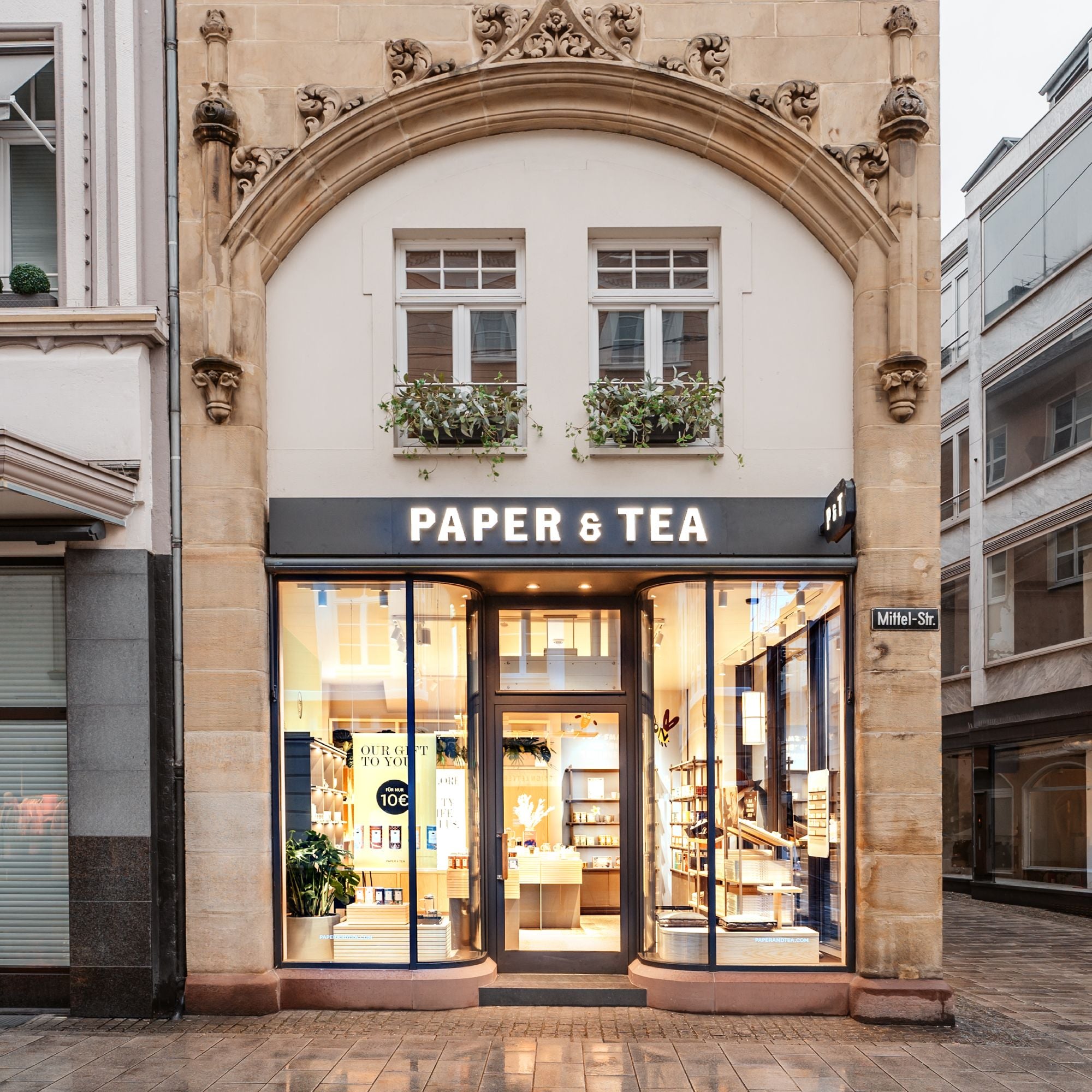 Eleganter PAPER & TEA Laden mit großen Glasfenstern und verziertem Sandsteinportal in der Mittelstraße.