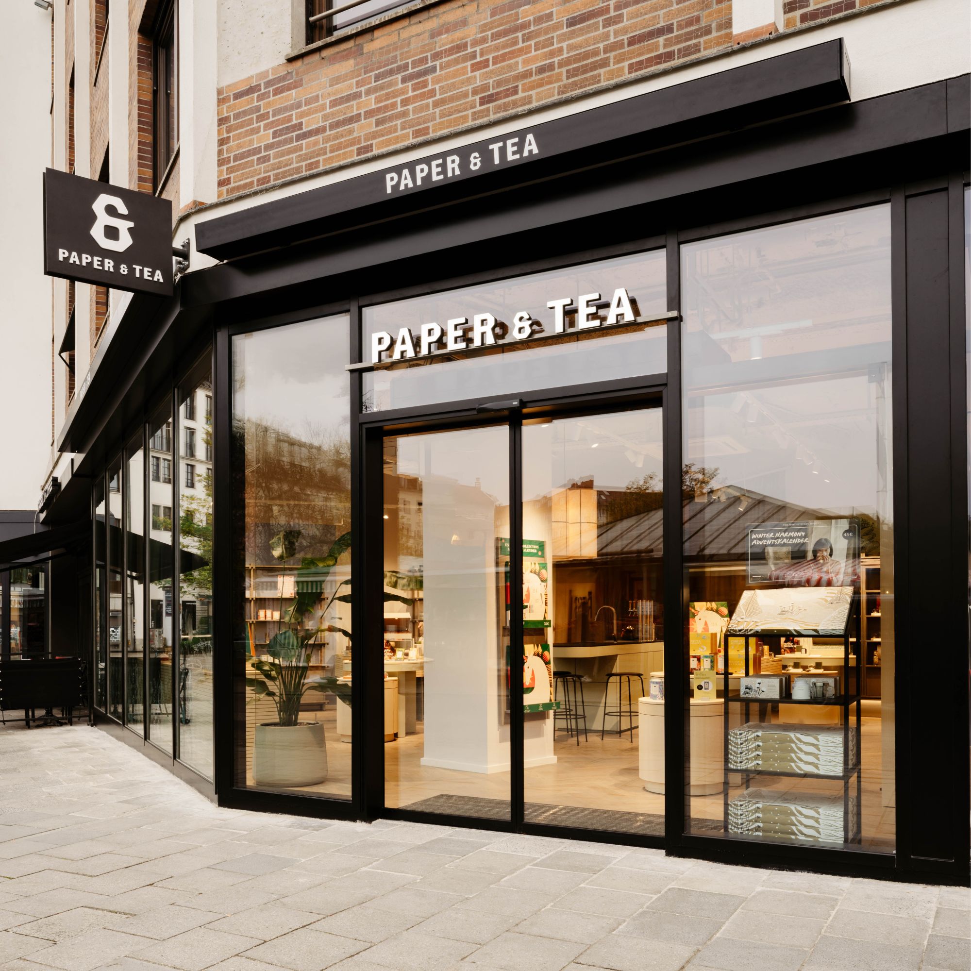 Moderner PAPER & TEA Laden mit schwarzer Fassade, großen Glasfenstern und Winter Harmony Adventskalender im Schaufenster.