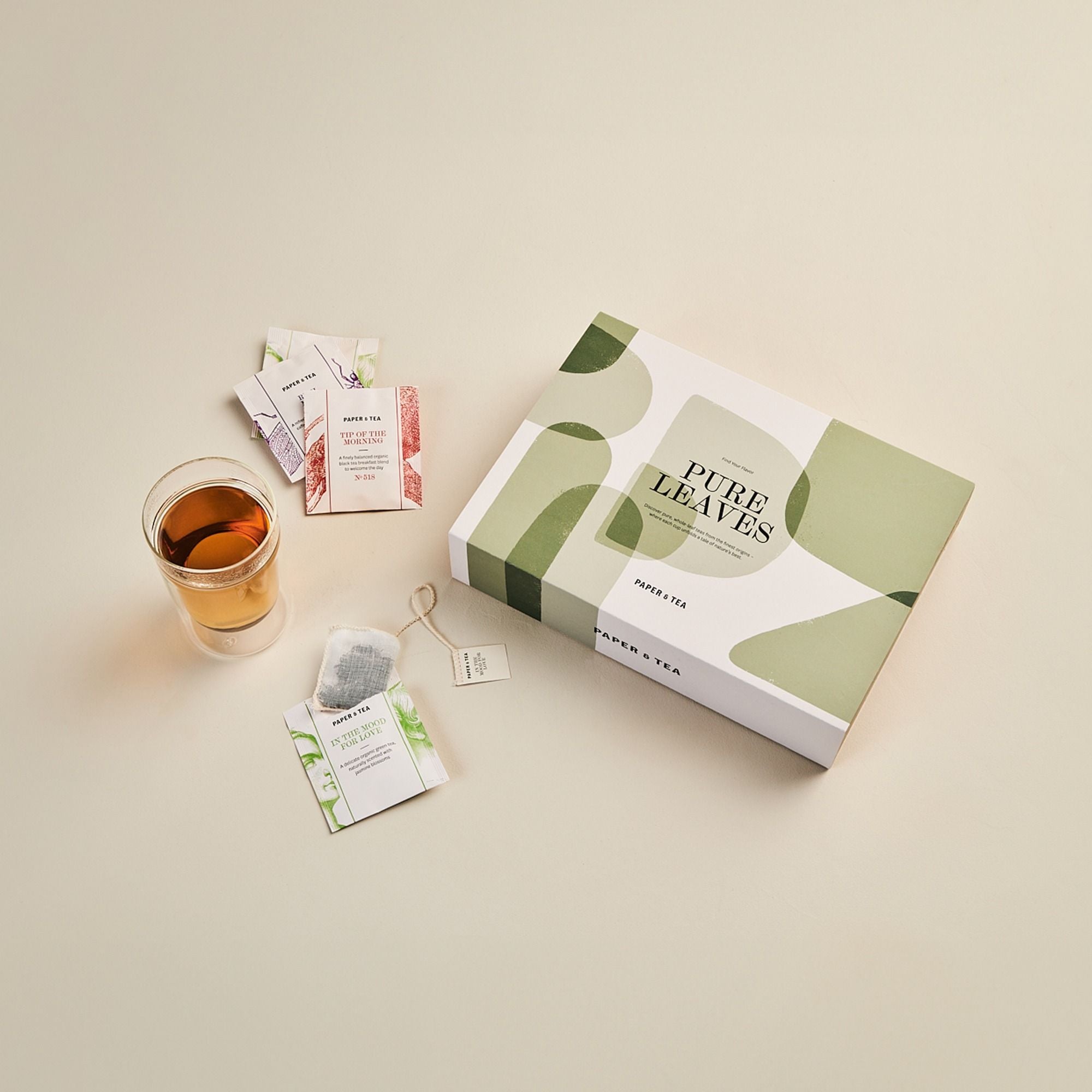 Elegante Tee-Komposition mit PURE LEAVES Box, Glas mit Tee und Bio-Teebeuteln Tip of the Morning & In the Mood for Love.