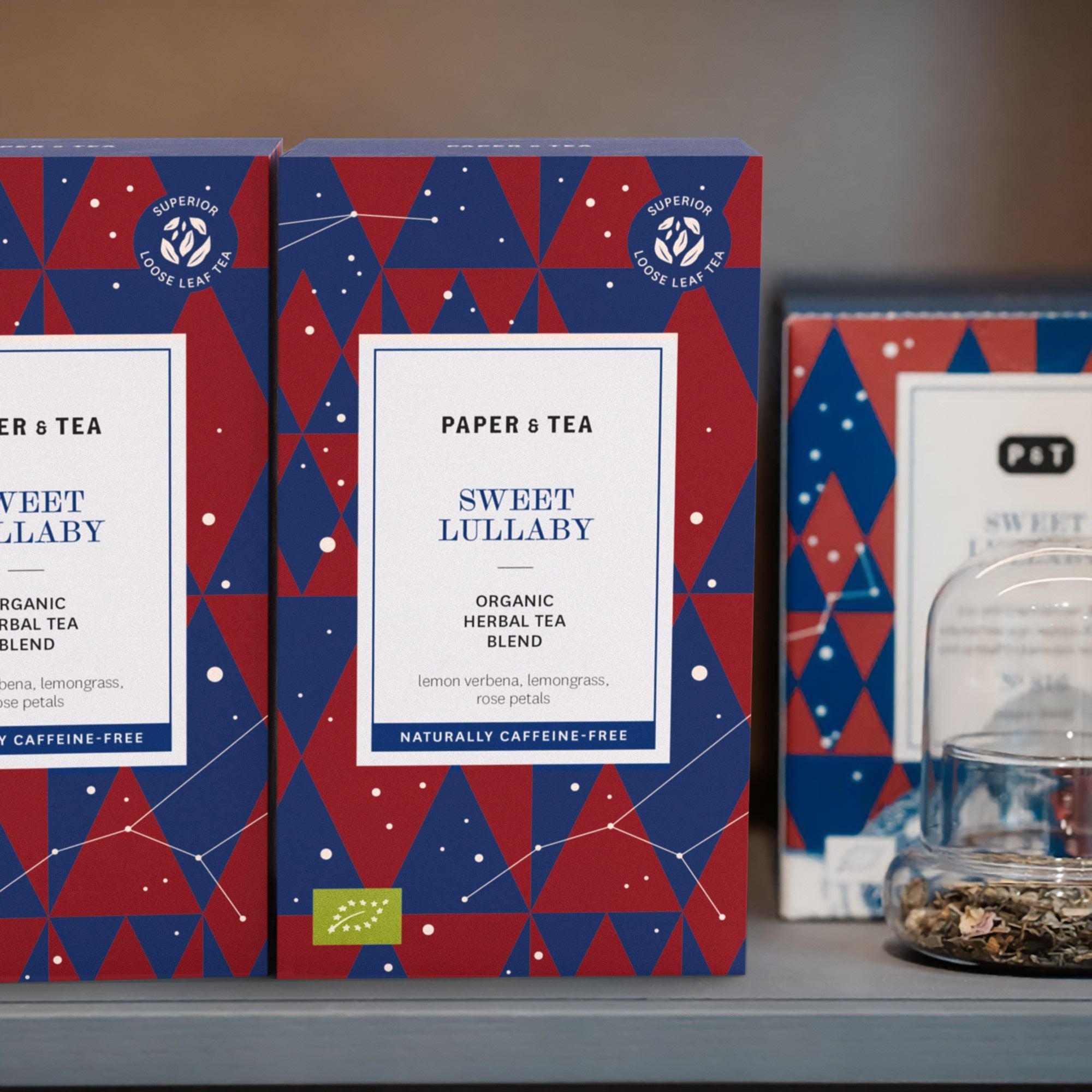 Drei Paper & Tea-Packungen mit geometrischen Mustern und Sweet Lullaby Kräutertee sowie lose Teeblätter.