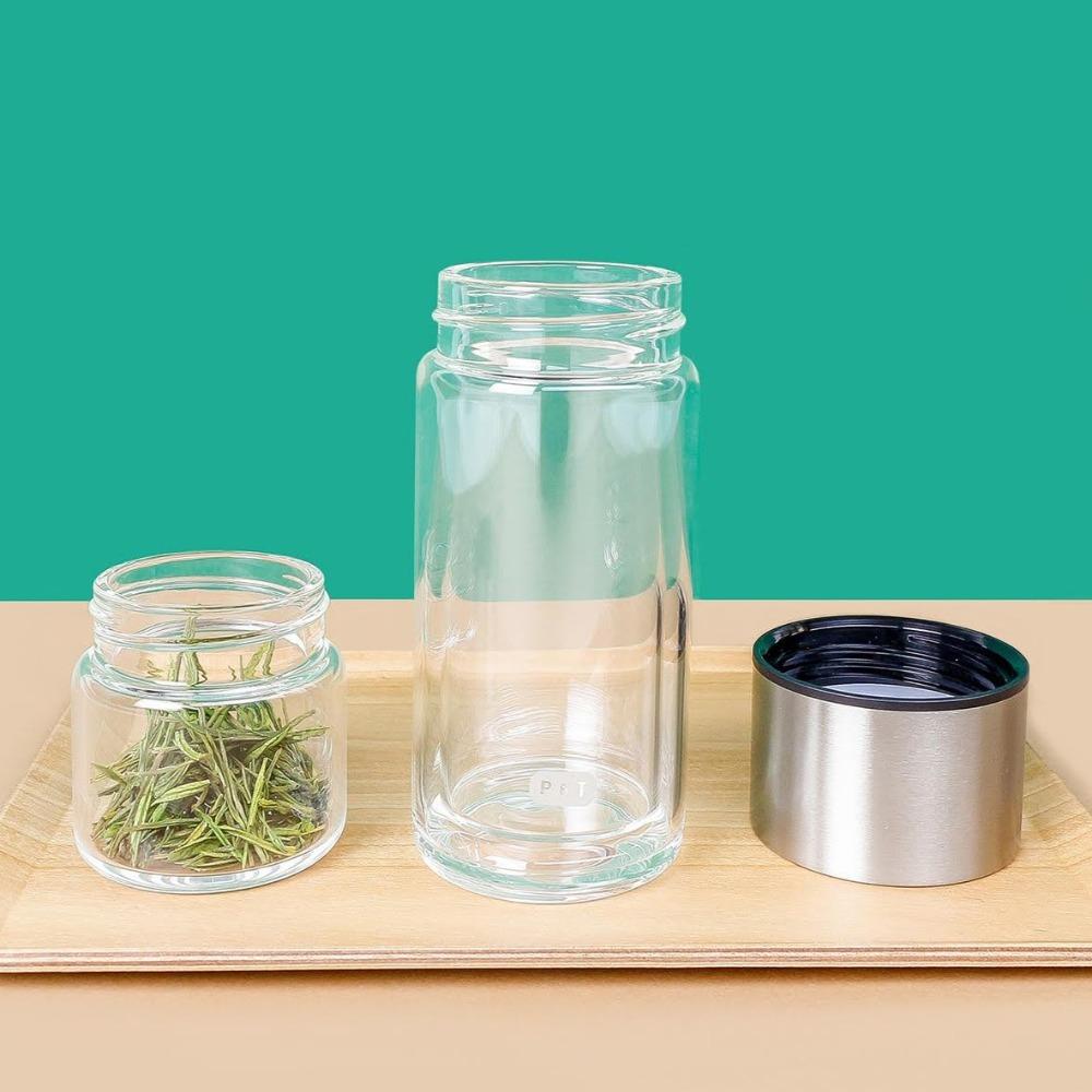 Holztablett mit zwei Glasbehältern: kleinerer mit grünen Kräutern, höherer mit 'P & T'-Beschriftung, neben einem metallicfarbenen Deckel.