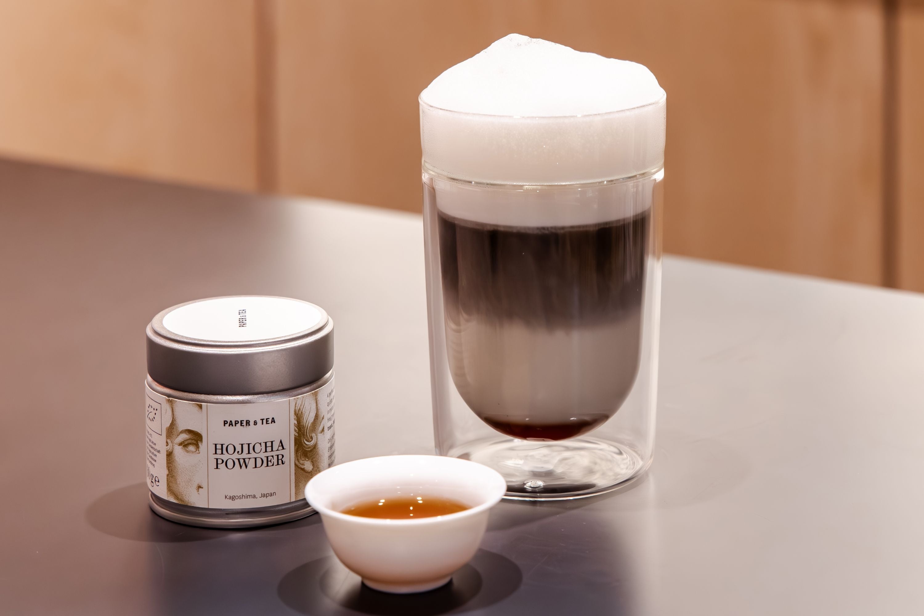 Metalldose mit Paper & Tea Hojicha Pulver, Glas mit dunklem Tee, Keramiktasse mit hellem Tee