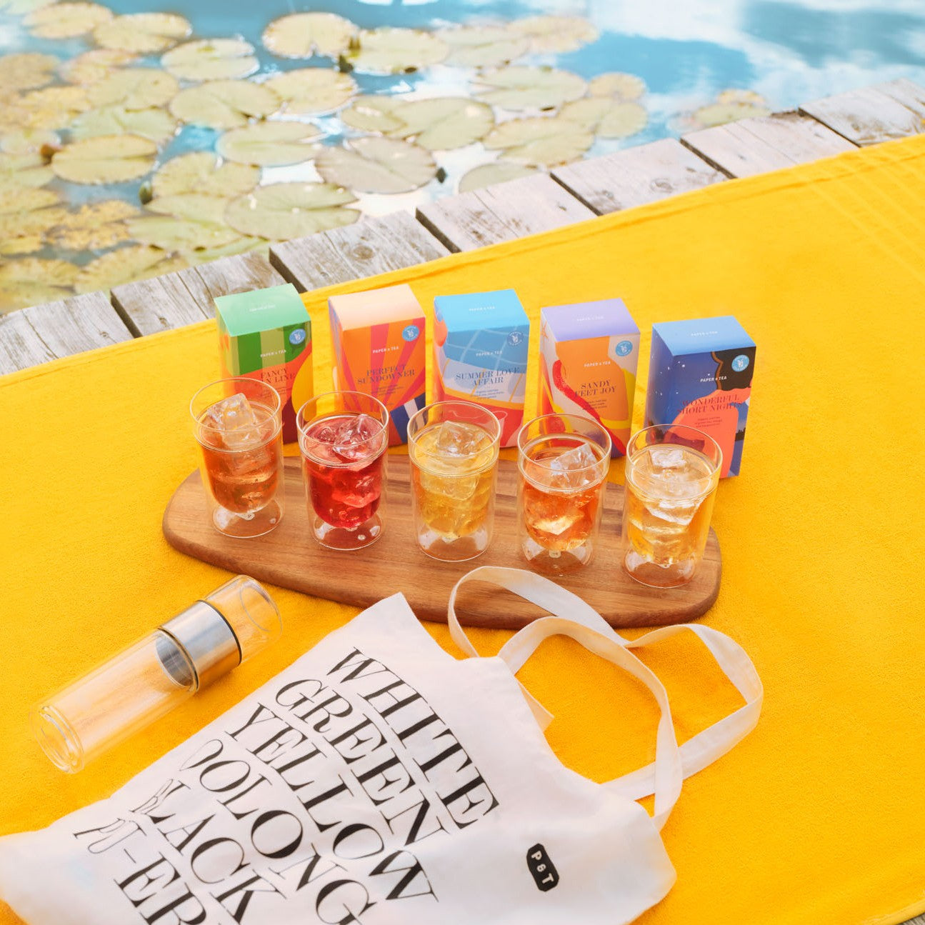 Bunte Paper & Tea Teeboxen, Eistee auf Holztablett, Tragetasche und Flasche am See mit Seerosen