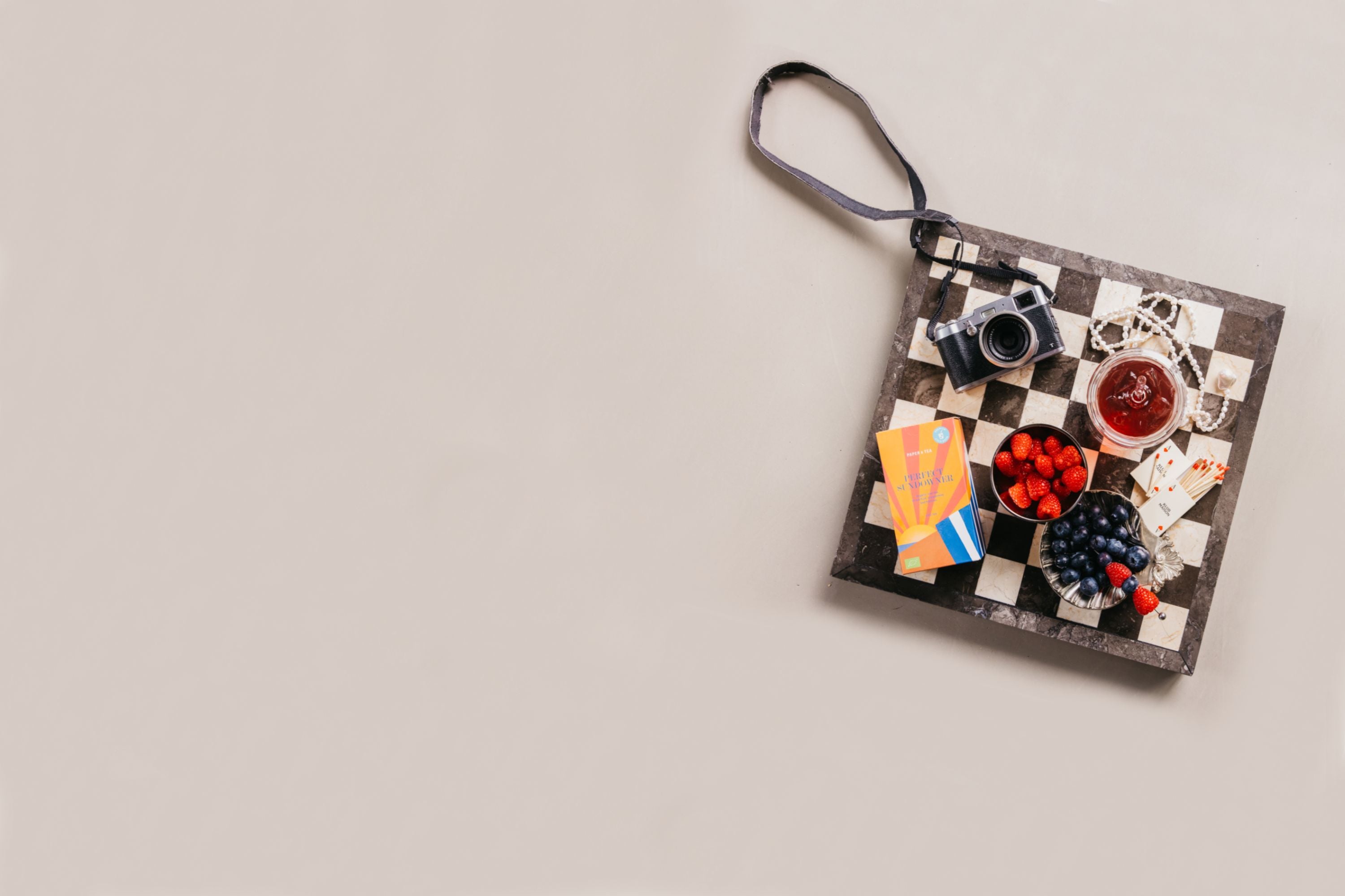 Quadratisches Tablett mit Kamera, Perlenschmuck, Beerenschalen, rotem Getränk und P&T Perfect Sundowner Box