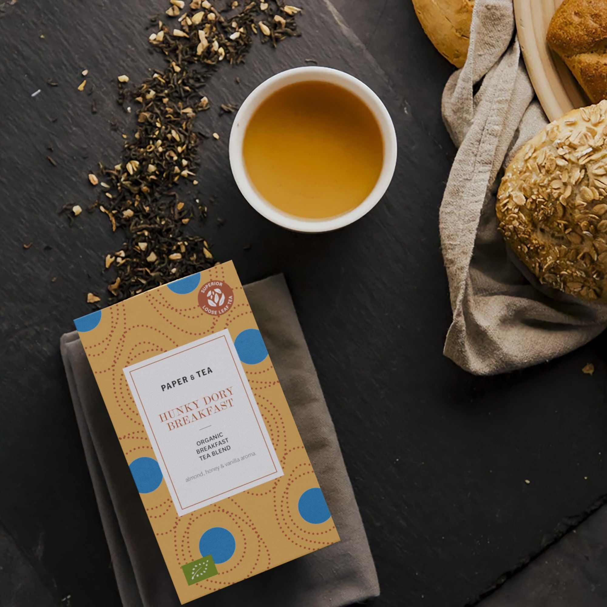 Hunky Dory Frühstücks-Bio-Tee mit Mandel, Honig und Vanille, Tasse Tee, lose Blätter und Haferbrötchen.