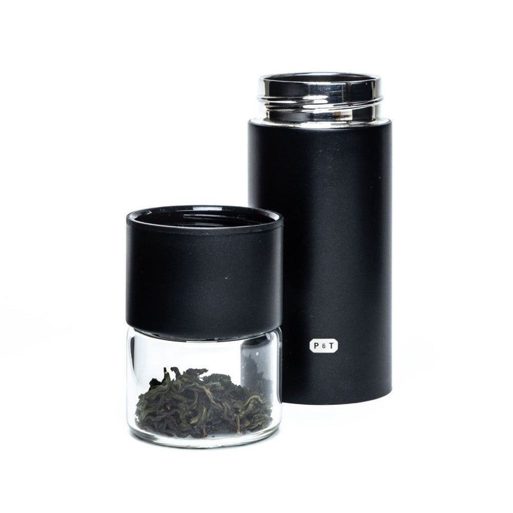 Kleine Glasdose mit Teeblättern neben großer schwarzer Teedose mit P & T Etikett und Schraubdeckel.