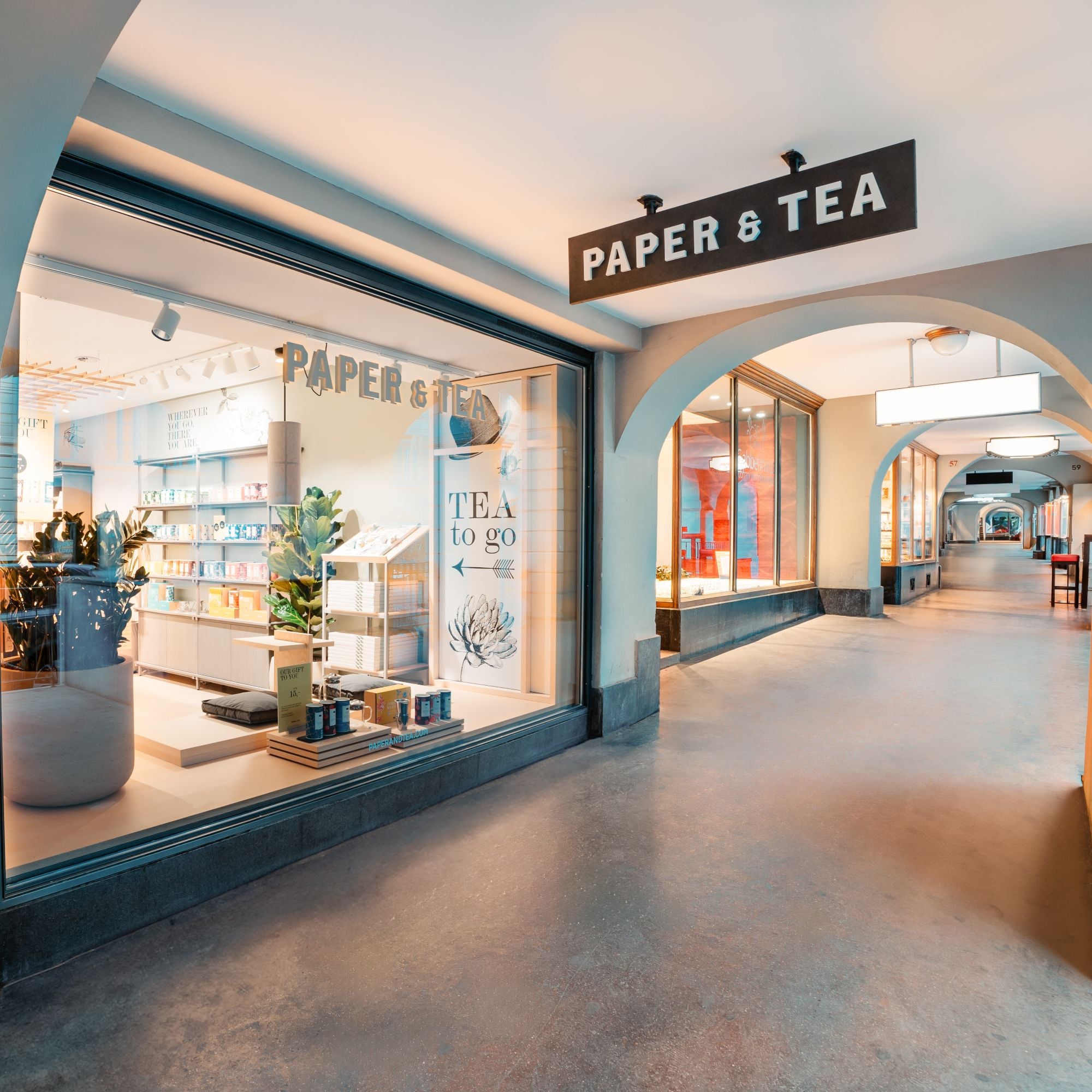 PAPER & TEA Filiale mit Schaufenster, Teeprodukten und beleuchtetem Passagenbogen, Hausnummern 57 und 59.