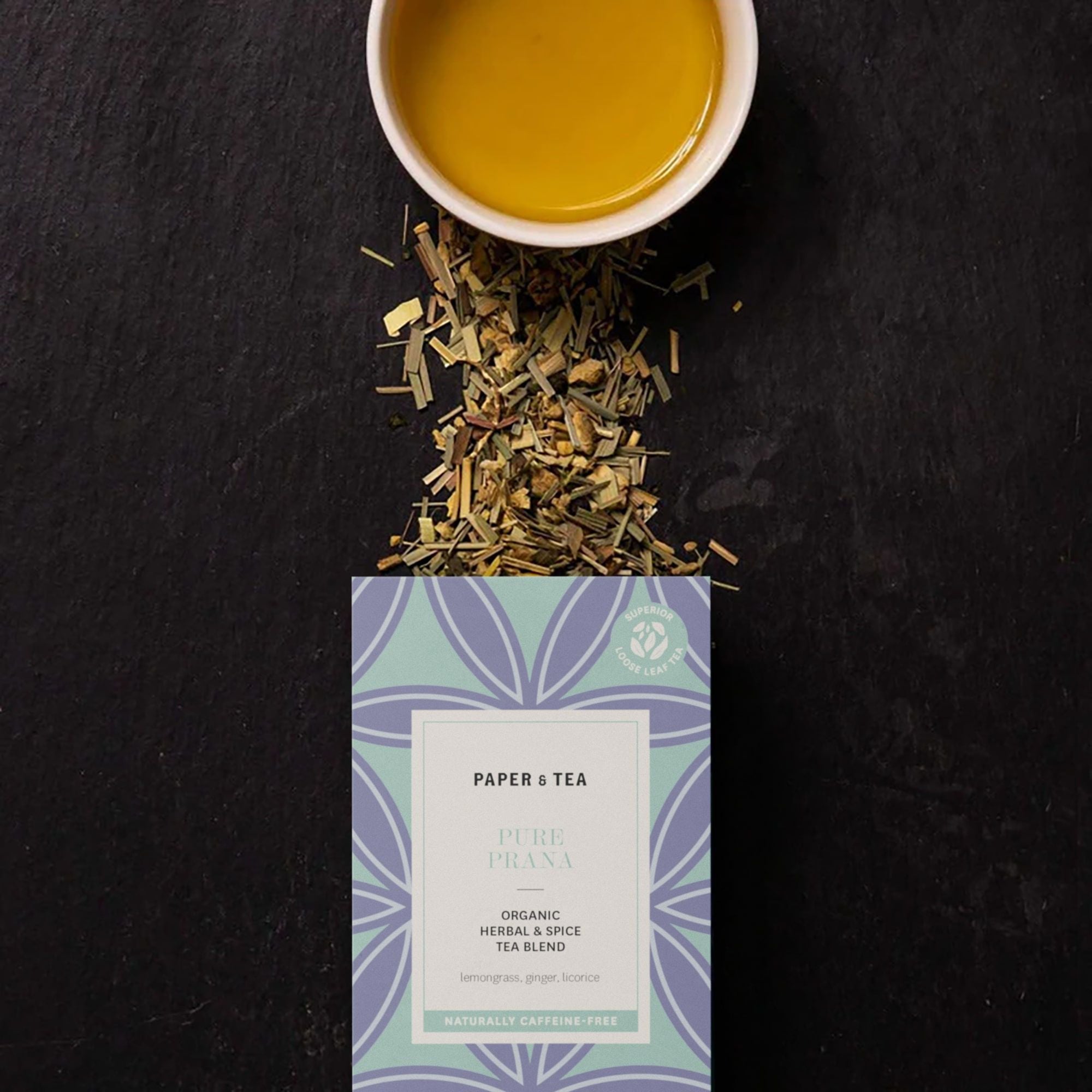 Blauer und grüner PURE PRANA Kräutertee in geometrischer Verpackung neben weißer Teetasse