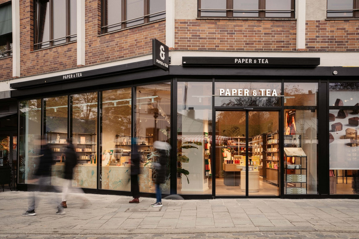 Eckladen von P&T mit großen Glasfenstern, schwarzem Rahmen und beleuchteten Regalen voller Premium-Tees.